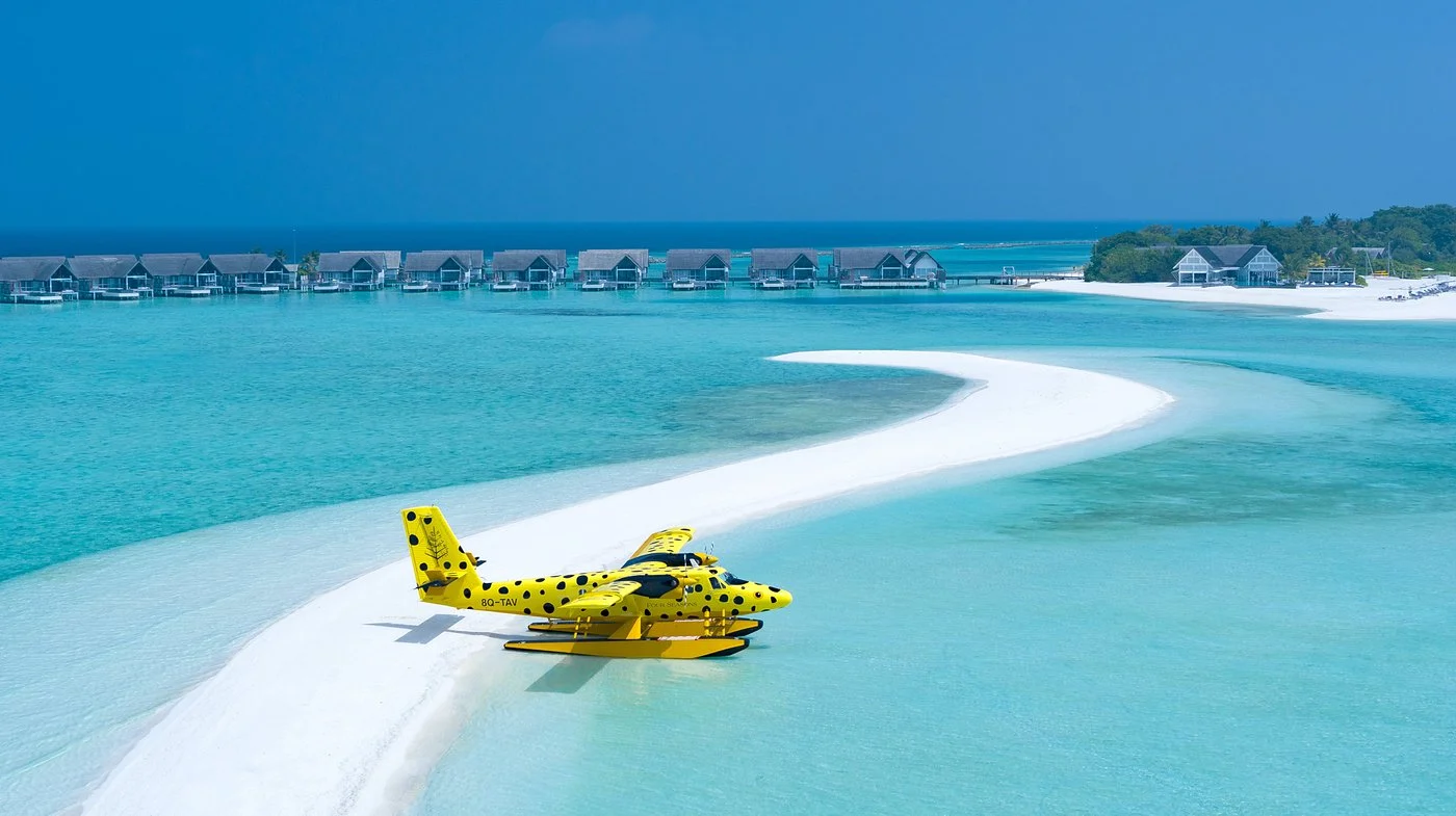 A seaplane on a white sandbar beside luxury overwater villas in the Maldives – Hummingbird Travel
